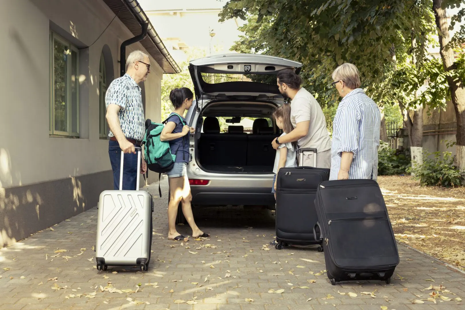 Smiling large family packing the car trunk with luggage for summer vacation, parents and little kid meeting with senior grandparents for their relaxing summer road trip together.